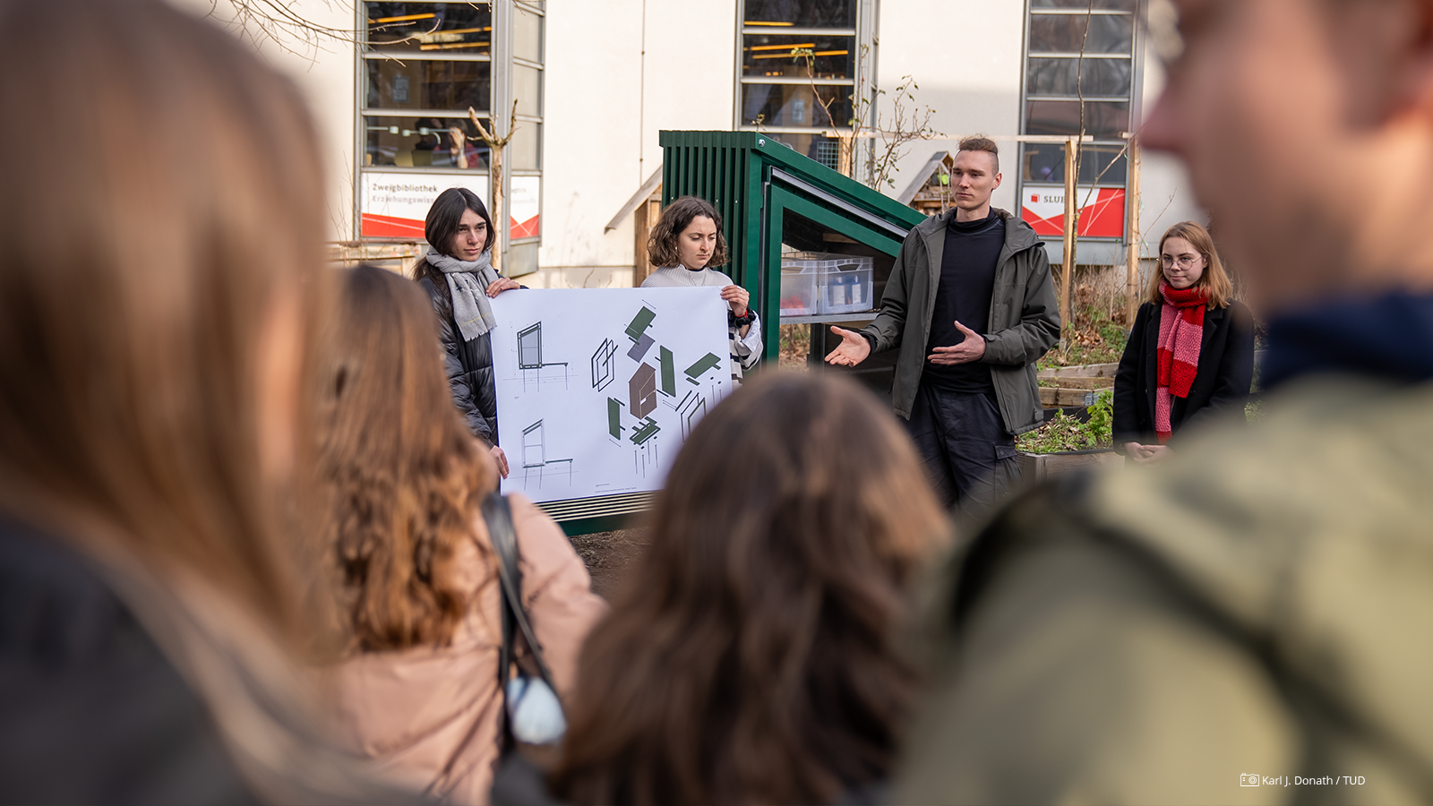 Foto von Studierenden, die ein großes Papier in der Hand halten, auf dem Entwürfe für den "Fairteiler" zu sehen sind. Foto von Studierenden, die ein großes Papier in der Hand halten, auf dem Entwürfe für den "Fairteiler" zu sehen sind.
