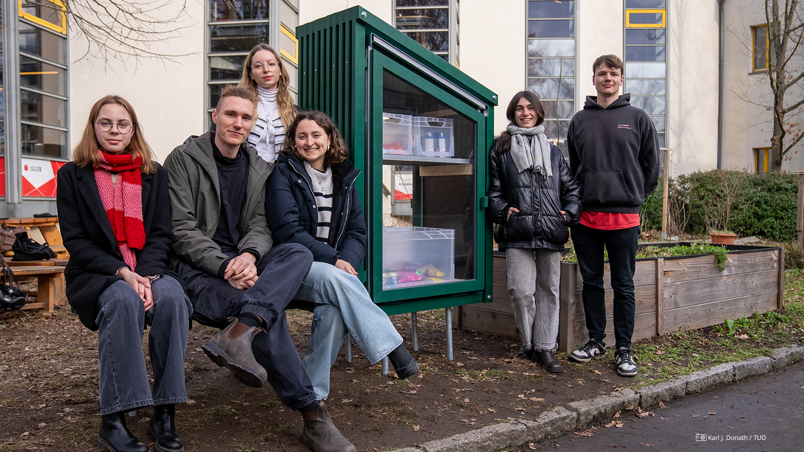Gruppenfoto von Studierenden vor dem "Fairteiler", den sie entworfen und gebaut haben. Der "Fairteiler" ist eine grüne Holzkonstruktion. Gruppenfoto von Studierenden vor dem "Fairteiler", den sie entworfen und gebaut haben. Der "Fairteiler" ist eine grüne Holzkonstruktion.